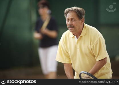 Active senior man in his 70s playing tennis.