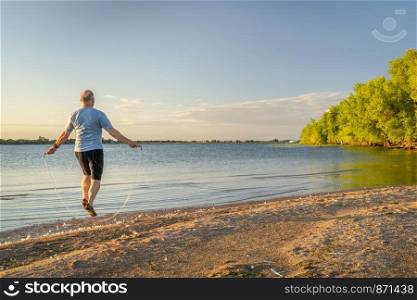 active senior man is jumping a heavy fitness jump rope on a lake beach, Boyd Lake State Park in northern Colorado