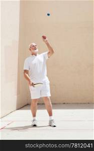 Active senior man tosses the racquetball in the air.