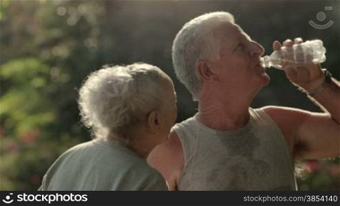 Active senior people, old man and woman talking and drinking water after exercising in park