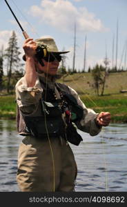 Active senior woman casting a fly-fishing rod in the Firehole River in Yellowstone Park.