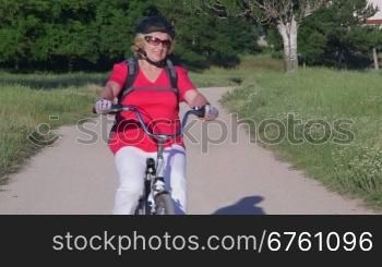 Active senior woman cycling in summer park