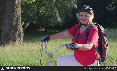 Active senior woman cyclist on bicycle looking at camera smiling