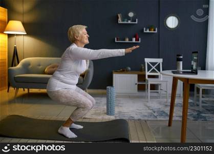 Active senior woman doing squats on yoga indoors. Home training and morning sport exercise activity. Senior woman doing squats exercising at home