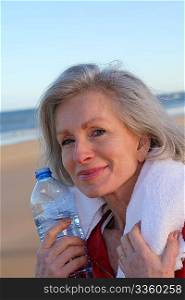 Active senior woman drinking water from bottle at the beach