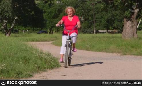 Active senior woman rides bicycle along the path in park