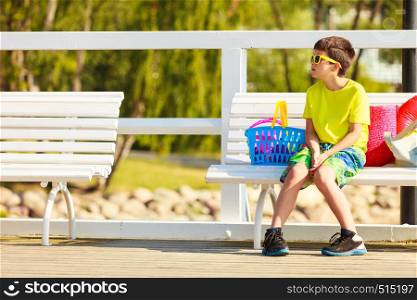 Active time on holidays concept. Young little boy sitting on white bench outdoor. Kid child with toys on summer holiday time.. Boy sitting on bench with toys.
