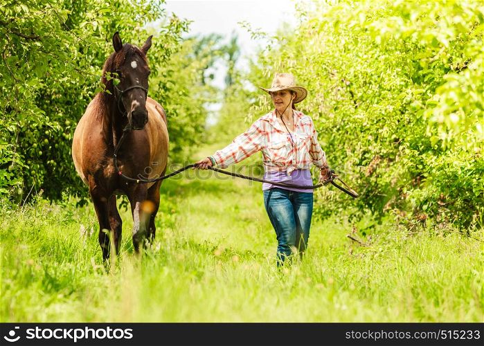 Active western cowgirl woman in hat walking with horse. American girl in countryside ranch.. Western cowgirl woman with horse. Sport activity