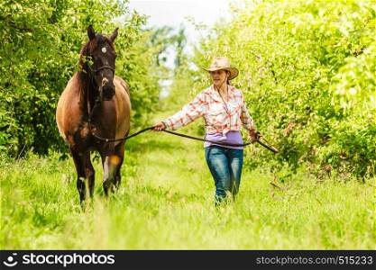 Active western cowgirl woman in hat walking with horse. American girl in countryside ranch.. Western cowgirl woman with horse. Sport activity