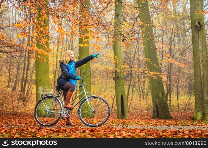 Active woman riding bike in autumn park.. Active woman riding bike bicycle in fall autumn park. Young girl in jacket and scarf relaxing. Healthy lifestyle and recreation leisure activity.