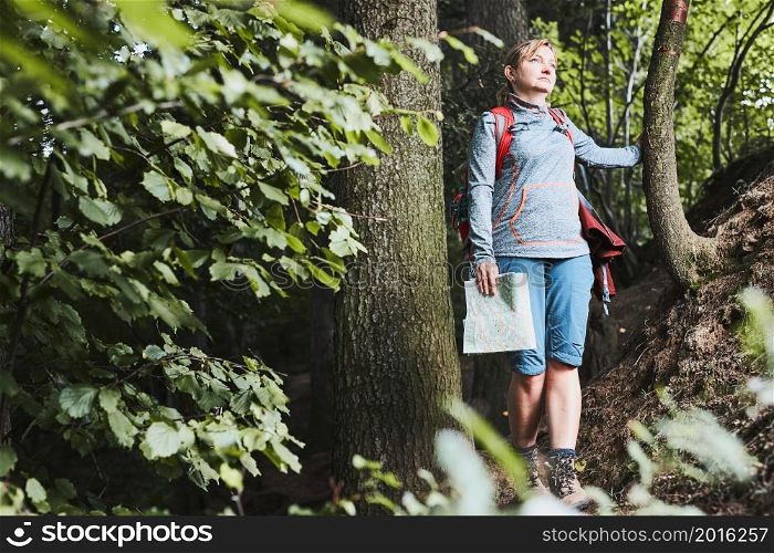 Active woman walking on forest path, actively spending summer vacation, carrying backpack, holding map