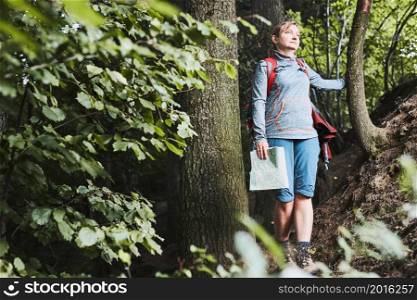 Active woman walking on forest path, actively spending summer vacation, carrying backpack, holding map