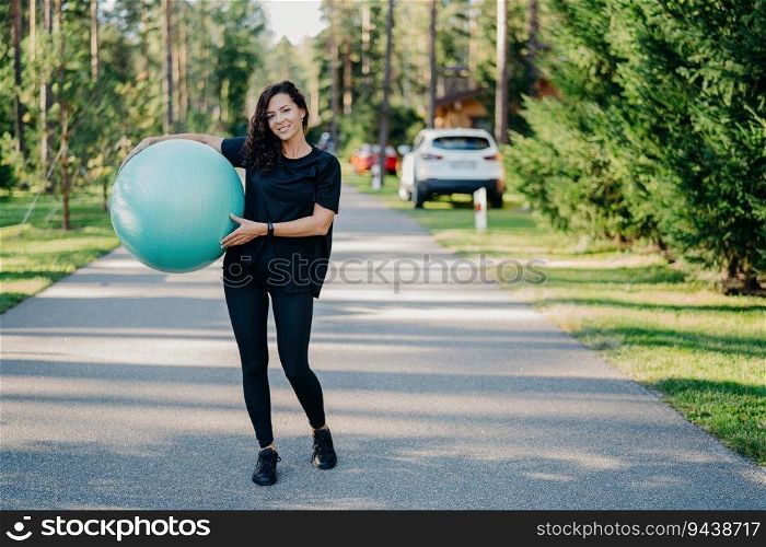 Active woman with fitness ball exercises outdoors, staying fit in sportswear. Embracing a healthy lifestyle near the forest. Gymnastics and aerobics.