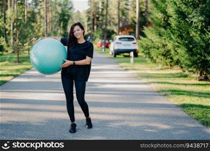 Active woman with fitness ball exercises outdoors, staying fit in sportswear. Embracing a healthy lifestyle near the forest. Gymnastics and aerobics.