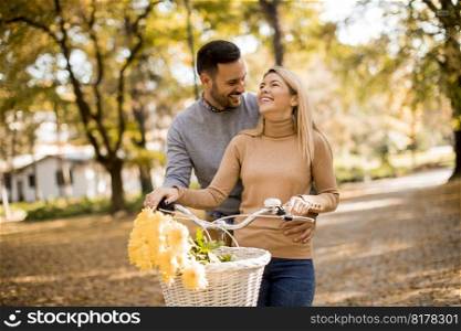 Active young couple enjoying together in romantic walk with bicycle in golden autumn park