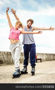 Active young people friends in training suit rollerskating outdoor. Happy woman and man with hands up.. Active young people friends rollerskating outdoor.