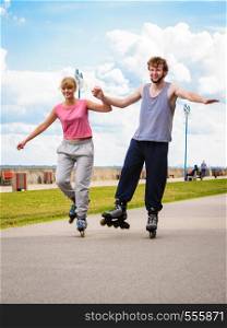Active young people friends in training suit rollerskating outdoor. Woman and man couple holding hands riding enjoying sport.. Active young people friends rollerskating outdoor.