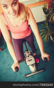 Active young woman working out on exercise bike stationary bicycle. Sporty girl training at home. Fitness and weight loss concept. High angle view.