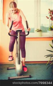 Active young woman working out on exercise bike stationary bicycle. Sporty girl training at home. Fitness and weight loss concept.