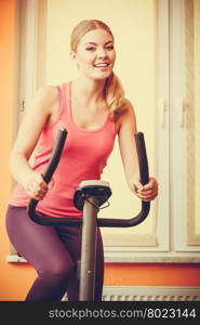 Active young woman working out on exercise bike stationary bicycle. Sporty girl training at home. Fitness and weight loss concept. Instagram filtered.