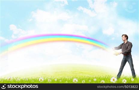 Add some color to your life!. Young man in casual splashing rainbow from bucket