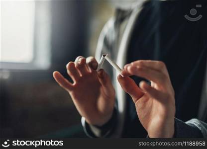 Addicted male person breaks a cigarette, blur background. Smoking addiction concept. Addicted male person breaks a cigarette