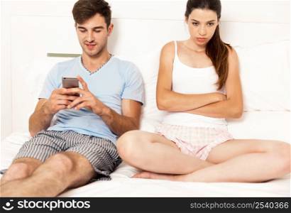 Addicted young man on bed with a cellphone while the woman looks angry