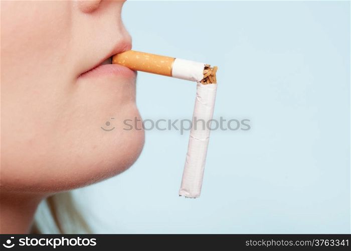 Addiction. Closeup of the broken cigarette in female mouth on blue. Quit smoking. Studio shot.
