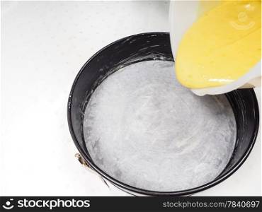 Adding cake mixture from white plastic bowl into a cake shape with baking paper
