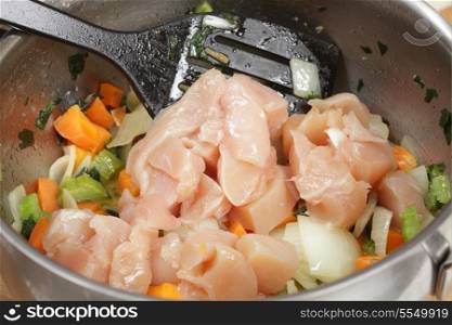 Adding diced chicken breasts to a risotto base of onion, carrot and celery that have been sweated in butter in a saucepan