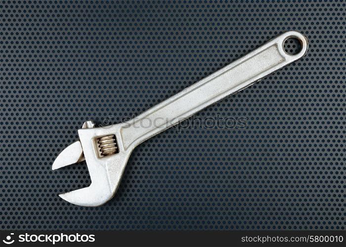 Adjustable wrench on a metallic background with perforation of round holes