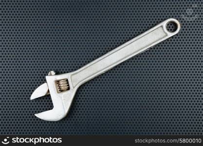 Adjustable wrench on a metallic background with perforation of round holes