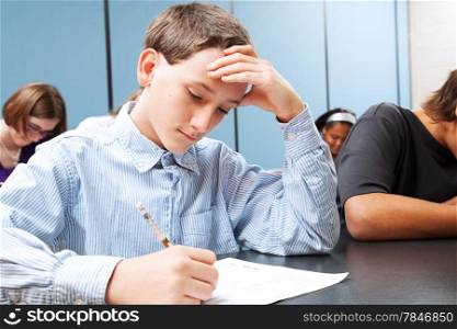 Adolescent middle school boy concentrats on a standardized test in school.