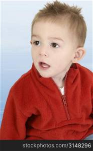 Adorable 1 year old boy in red sweater against blue background.