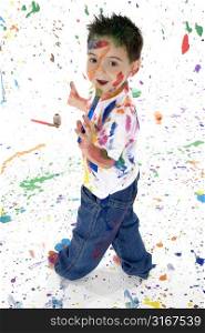 Adorable 3 year old boy covered in bright paint. Full body standing.
