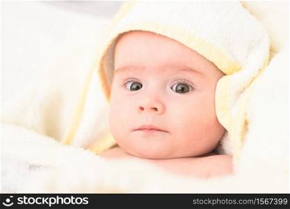 Adorable 6 months old Baby girl infant on a bed on her belly with head up looking into camera with her big eyes. Natural bedroom light.. Adorable 6 months old Baby girl infant on a bed on her belly with head up looking into camera with her big eyes. Natural light.