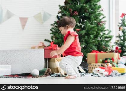Adorable 8 months Asian baby girl having fun playing ball toy, crawling on floor near a Christmas tree, among gift boxes, dolls and toys at home for celebrate holiday