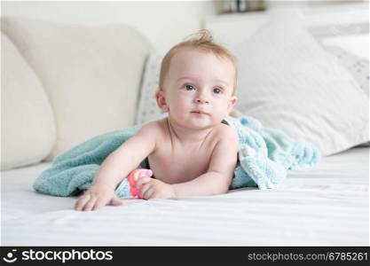 Adorable 9 months old baby on bed under blue towel after having shower