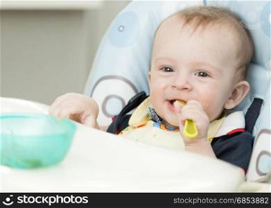 Adorable 9 months old boy eating in highchair at kitchen