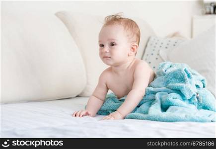 Adorable baby boy after shower covered in blue blanket on sofa at living room