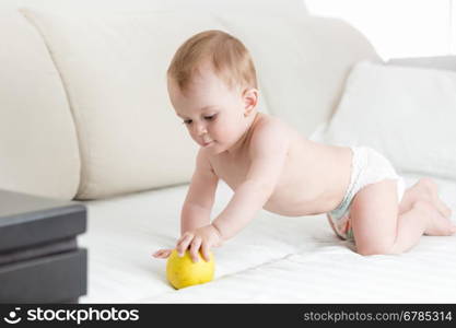 Adorable baby boy crawling on bed and reaching for apple