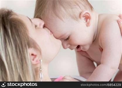 Adorable baby boy crawling on mothers belly on bed
