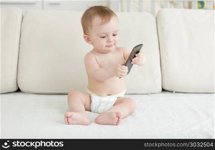 Adorable baby boy in diapers sitting on sofa and using smartphone. Baby boy in diapers sitting on sofa and using smartphone