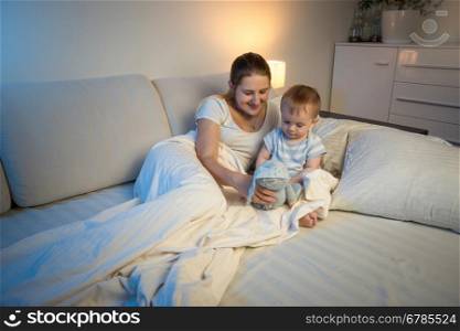 Adorable baby boy playing on bed at late night with his mother