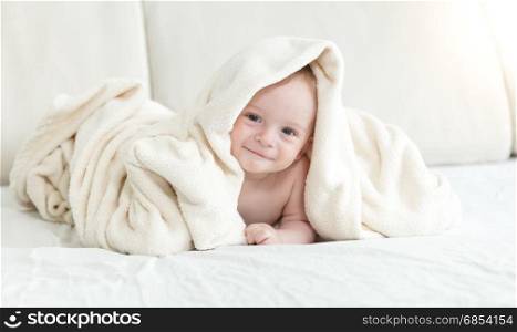 Adorable baby boy sitting on bed and covering in blanket
