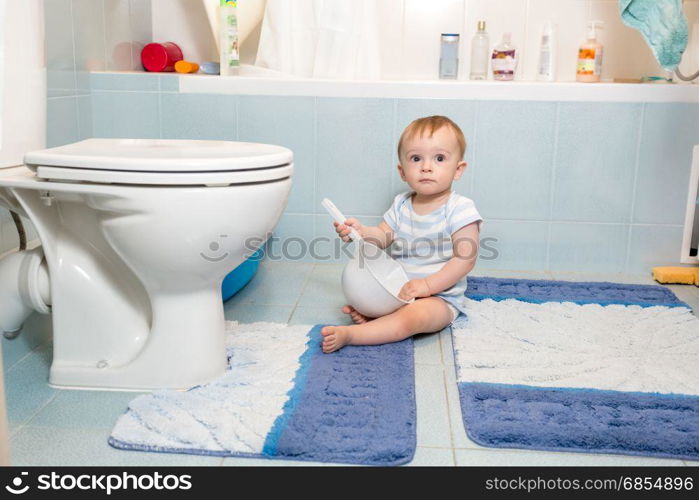 Adorable baby boy sitting on floor at bathroom