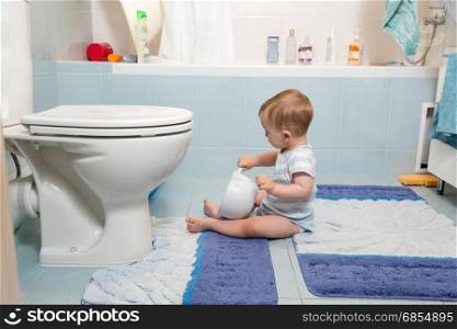 Adorable baby boy sitting on floor at bathroom and playing with toilet paper