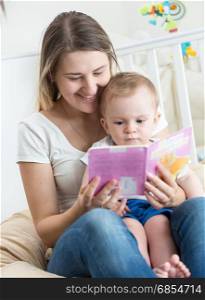 Adorable baby boy sitting on mothers lap and reading book