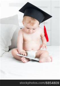 Adorable baby boy wearing graduation cap and using digital tablet