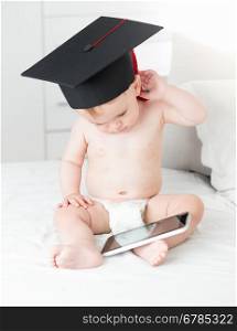 Adorable baby boy wearing graduation cap and using digital tablet. Concept of baby genius